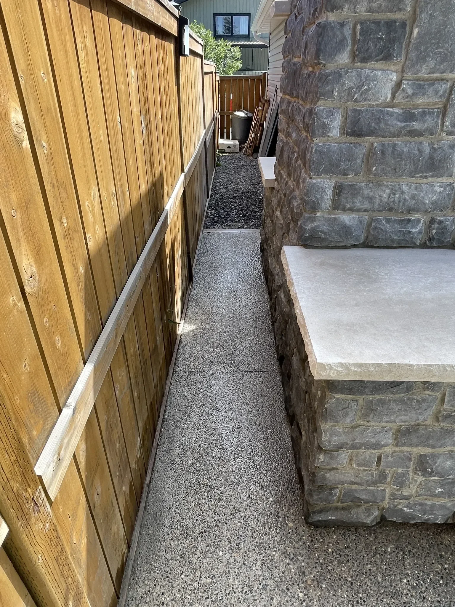 Narrow exposed aggregate concrete walkway poured along a side yard, providing a durable, low-maintenance access path with a clean, modern finish.