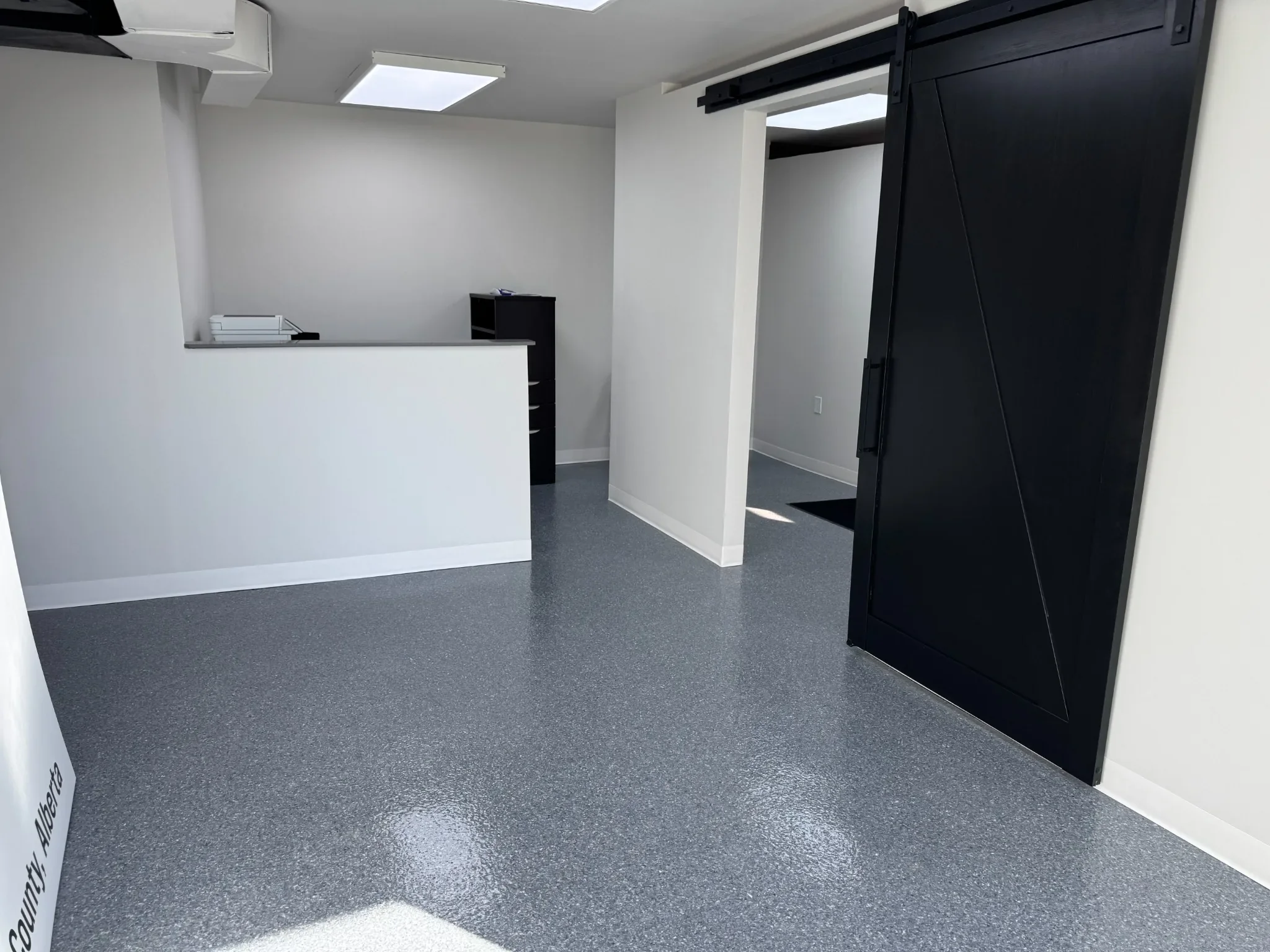 Modern commercial interior featuring a durable grey epoxy floor, clean white walls, and a sleek black barn door—ideal for offices, studios, and professional workspaces in Calgary.