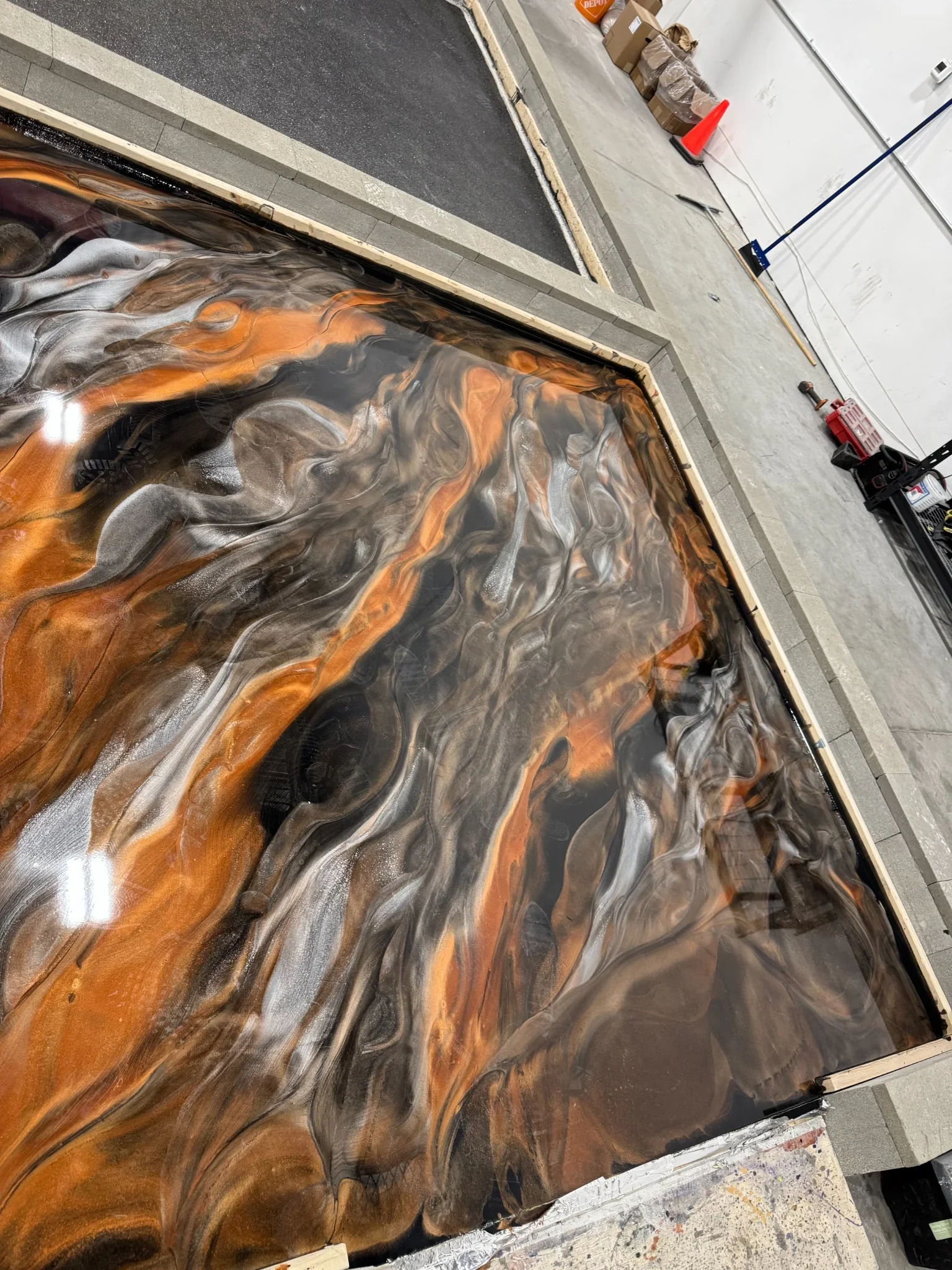 Custom metallic epoxy floor renovation featuring a high-gloss finish with flowing bronze, black, and silver tones, creating a durable and visually striking surface.
