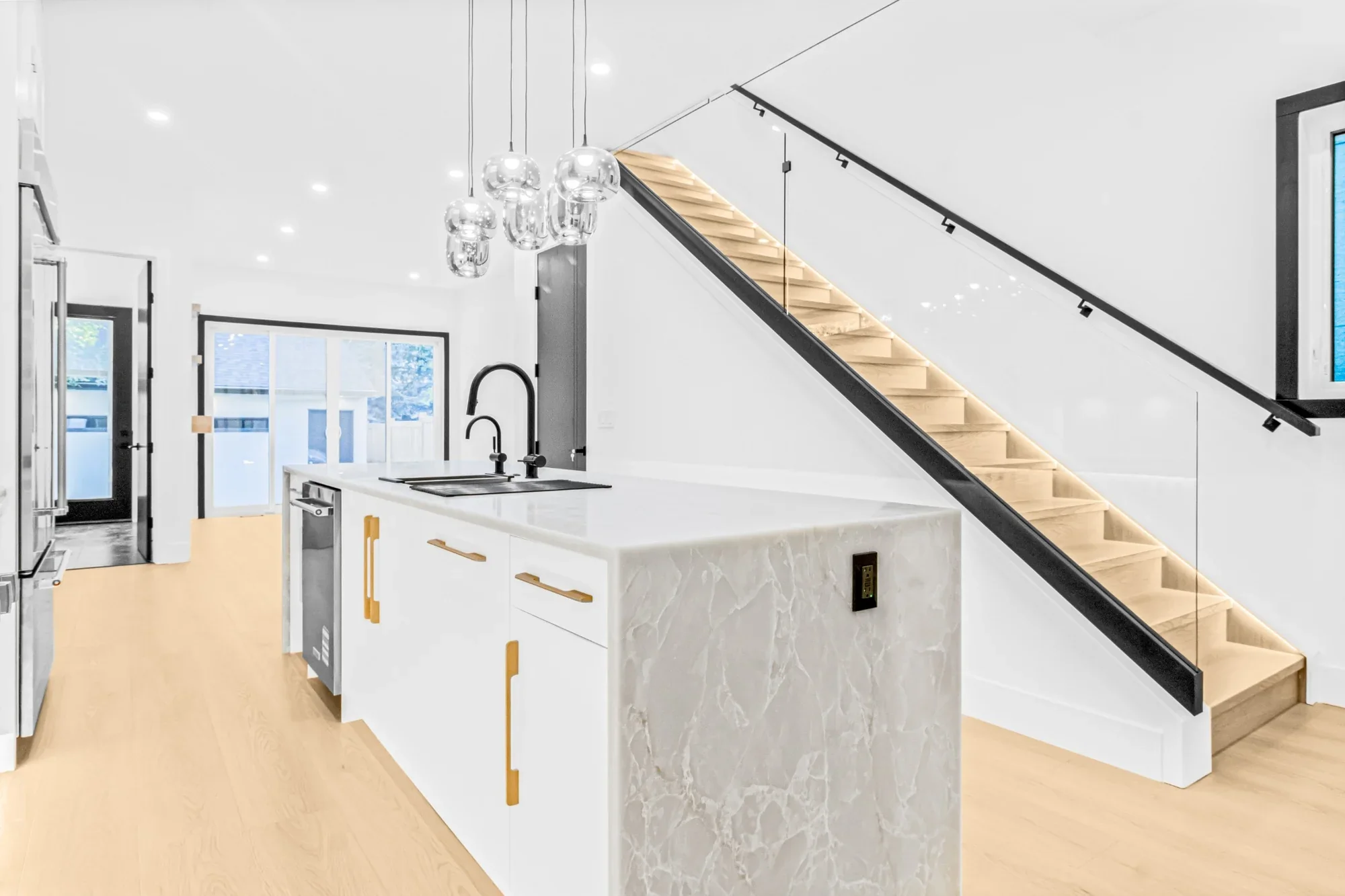 Modern home renovation featuring a custom kitchen island with waterfall stone countertops, black fixtures, pendant lighting, and a floating wood staircase with glass railing.