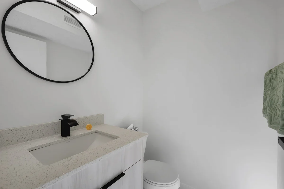 Modern bathroom renovation in Calgary with a custom vanity, quartz countertop, matte black fixtures, round mirror, and clean contemporary finishes completed by Da Vinci Contracting.