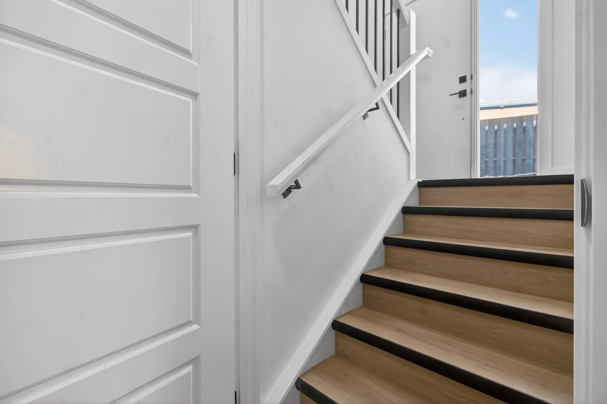 Modern staircase renovation featuring wood stair treads with black nosing, clean white railings, and contemporary trim detailing.