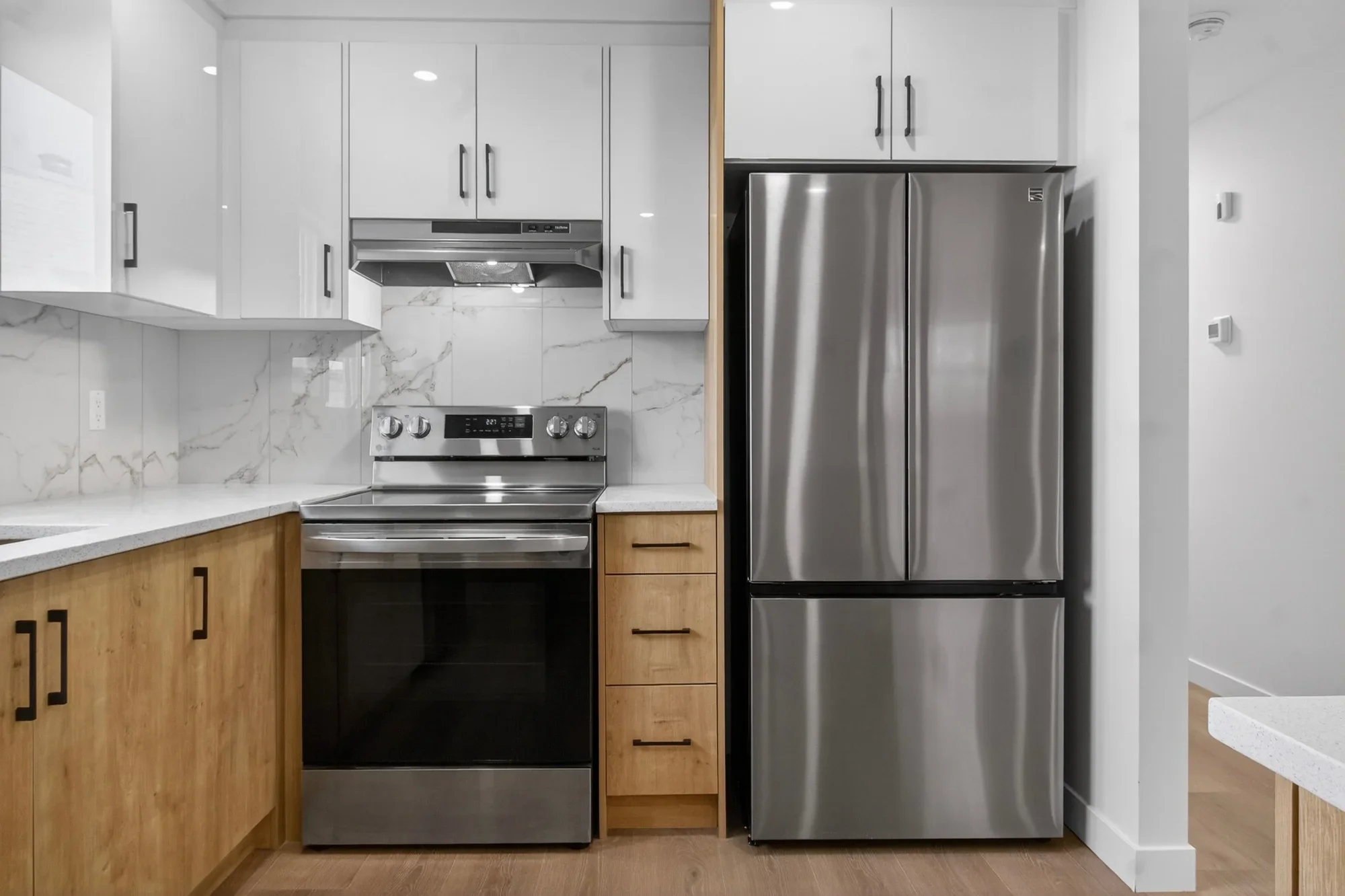 Detail view of a basement kitchen renovation showcasing stainless steel appliances, quartz countertops, marble-style backsplash, and custom cabinetry with modern hardware.