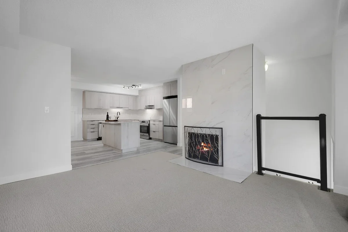 Open-concept home renovation in Calgary showcasing a custom marble fireplace, modern kitchen with a central island, luxury vinyl plank flooring, and bright contemporary finishes completed by Da Vinci Contracting.