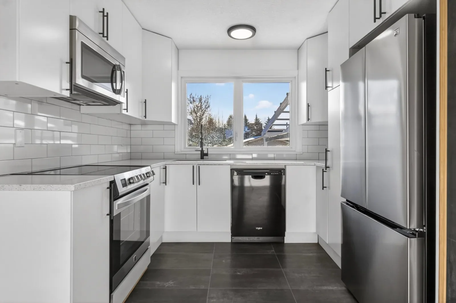 Modern kitchen renovation with white cabinetry, quartz countertops, stainless steel appliances, and subway tile backsplash in a Calgary home.