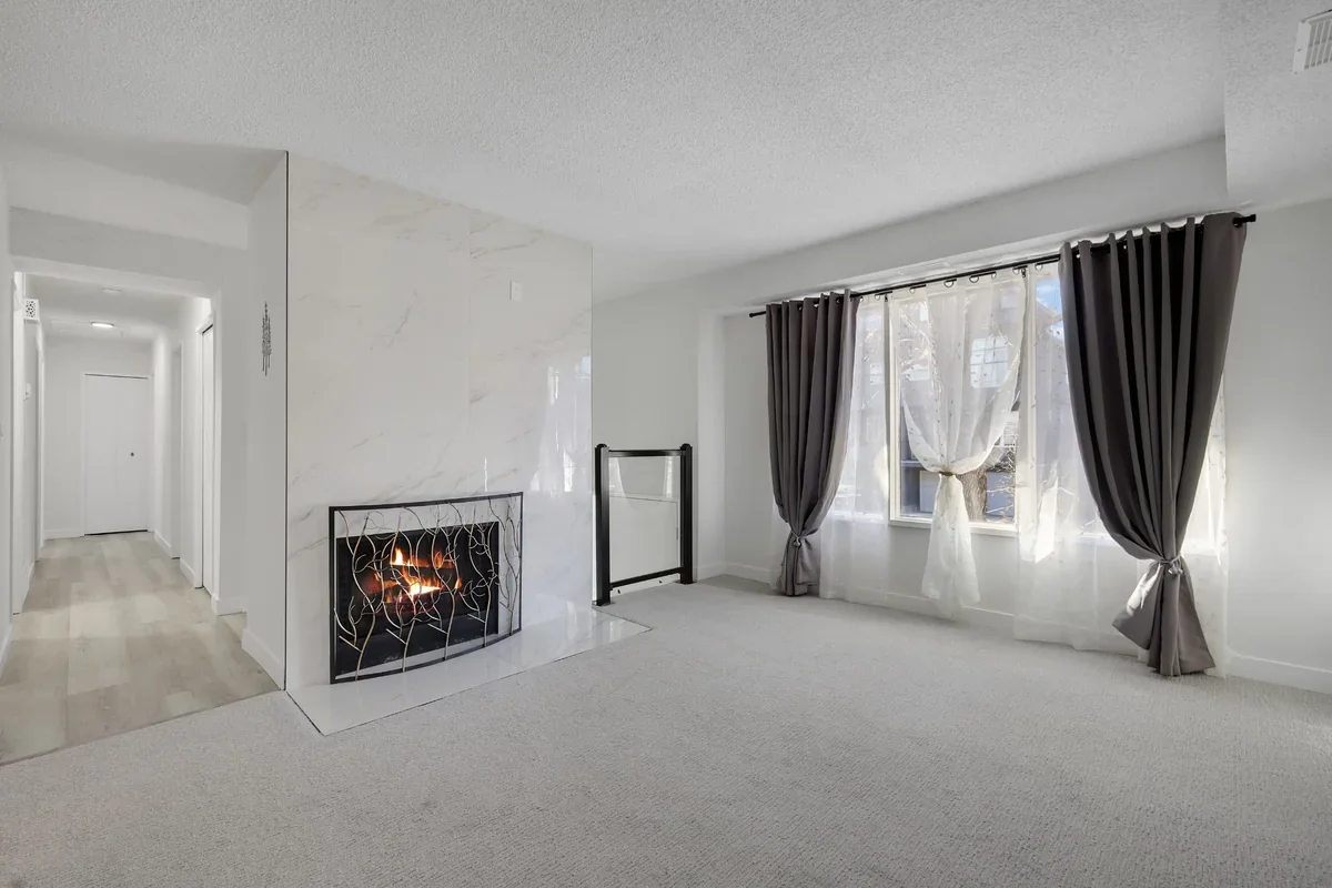 Modern living room renovation in Calgary showcasing a custom floor-to-ceiling marble fireplace, fresh paint, new carpet, large windows, and premium contemporary finishes completed by Da Vinci Contracting.