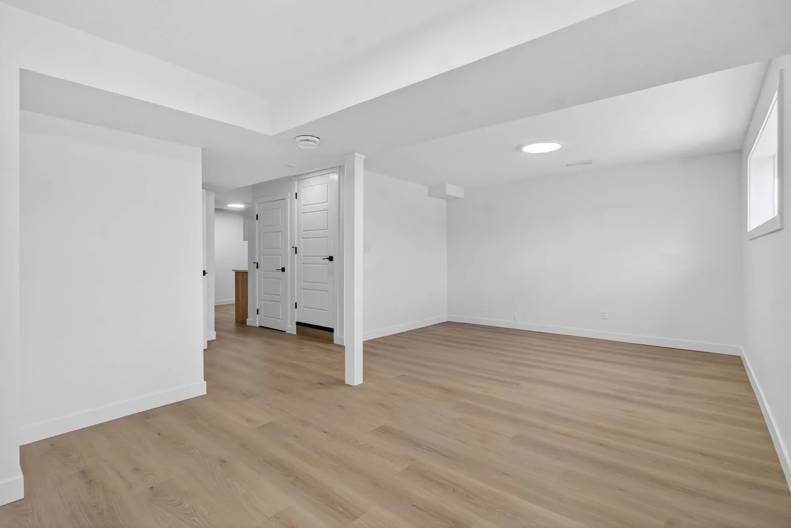 Modern basement renovation in Calgary featuring vinyl plank flooring, recessed lighting, white walls, and finished support columns