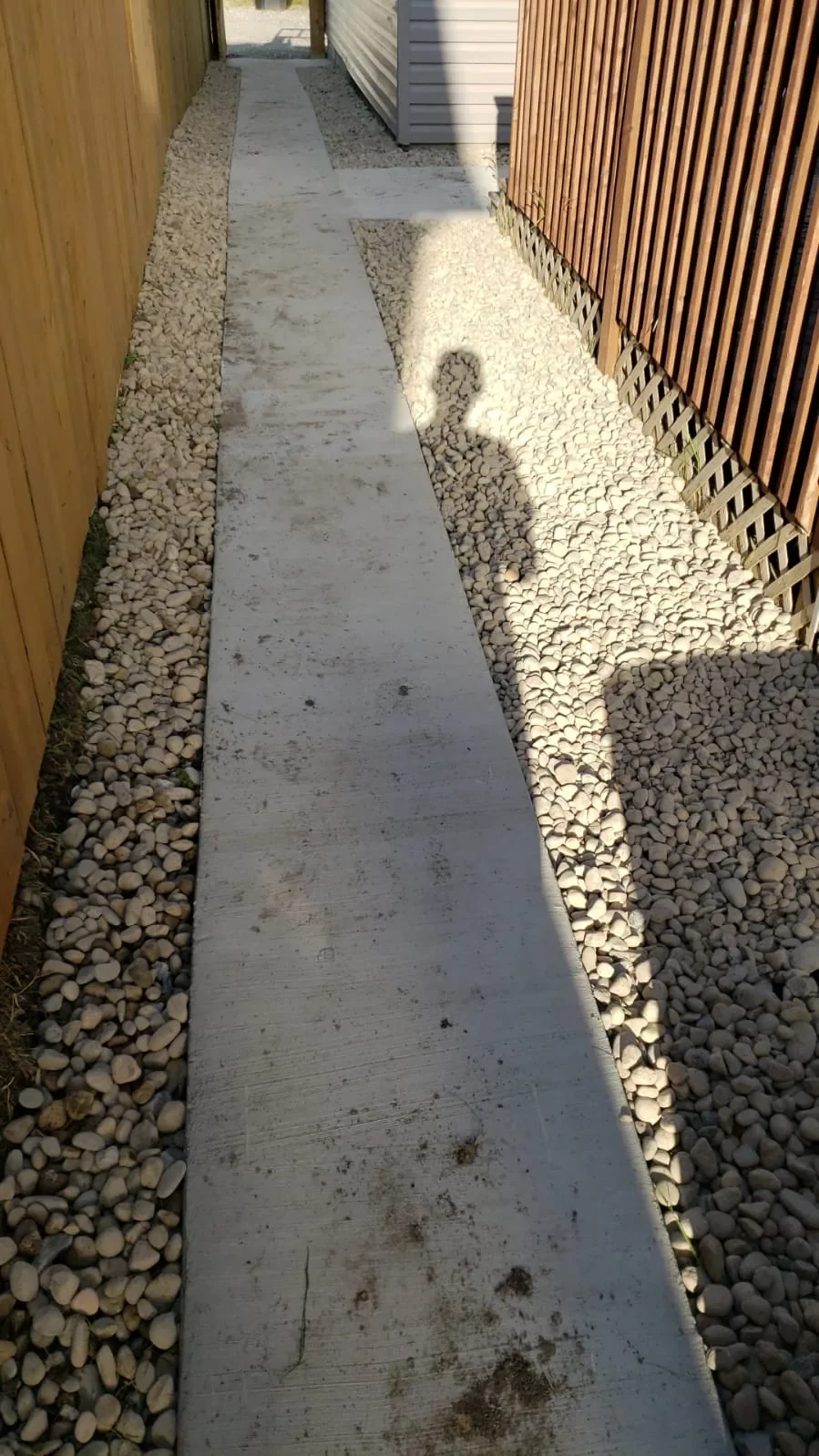 Straight-pour concrete side yard walkway installed for durability and low maintenance, paired with decorative rock for clean drainage and a polished finish.