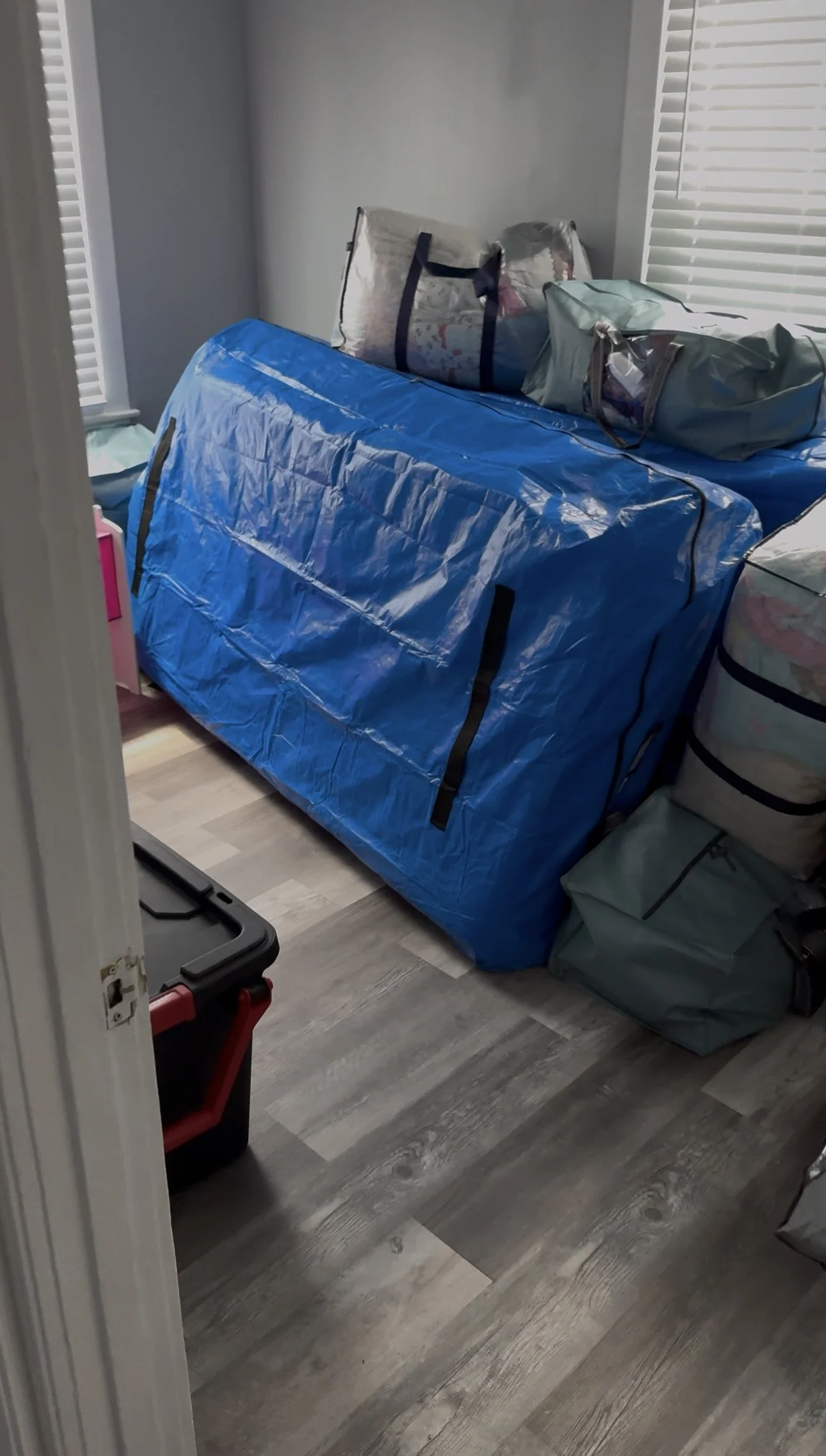 Room with packed bags, duffel bags, and plastic storage bins, possibly prepared for travel or moving.
