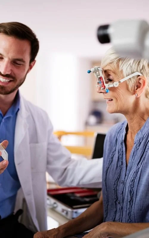 A female patient wearing a headlamp and glasses sitting at a dental or medical examination table with a doctor.
