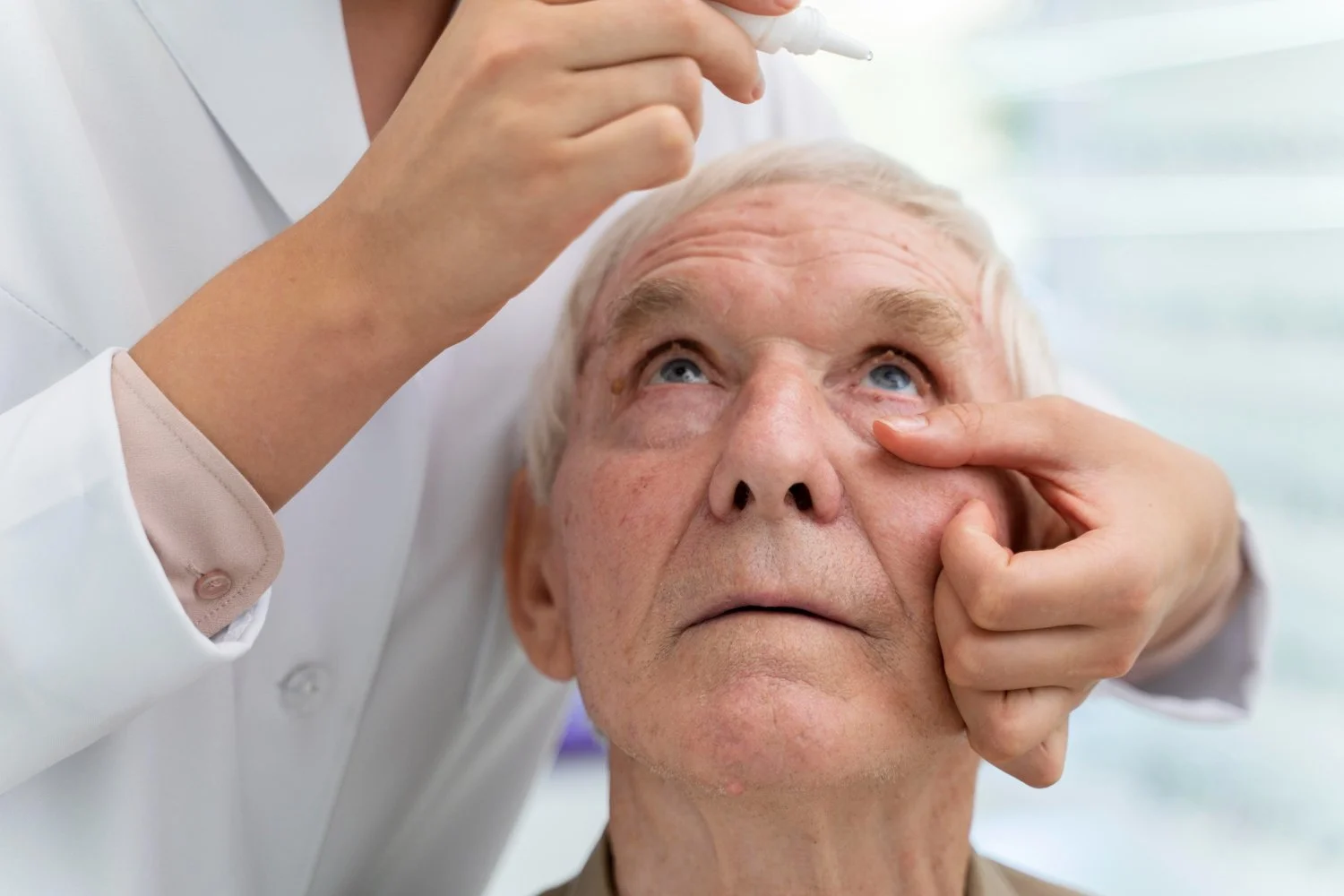 A healthcare professional examing an elderly man's eye in a clinical setting.