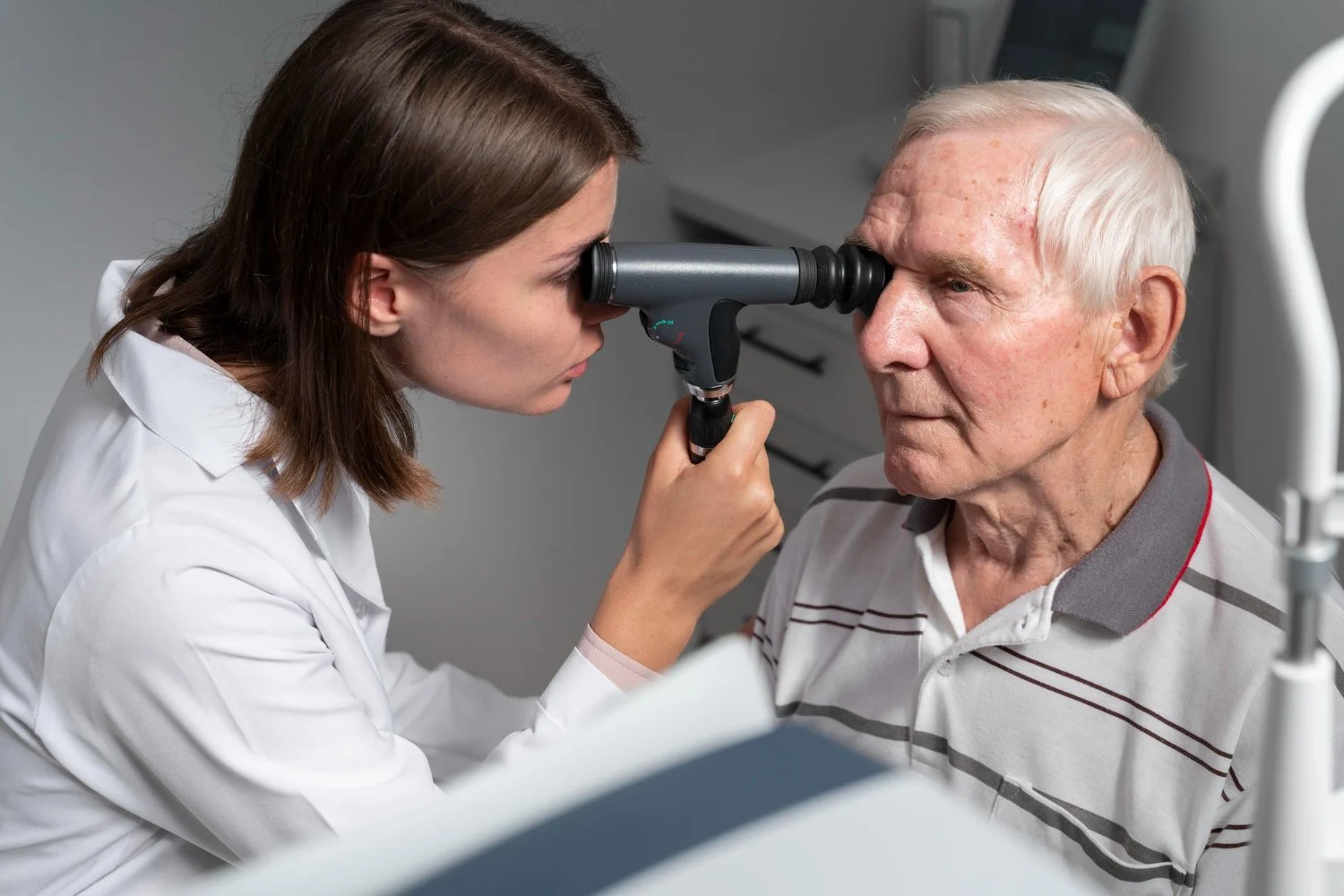 A healthcare professional using an ophthalmoscope to examine an elderly man's eye in a medical setting