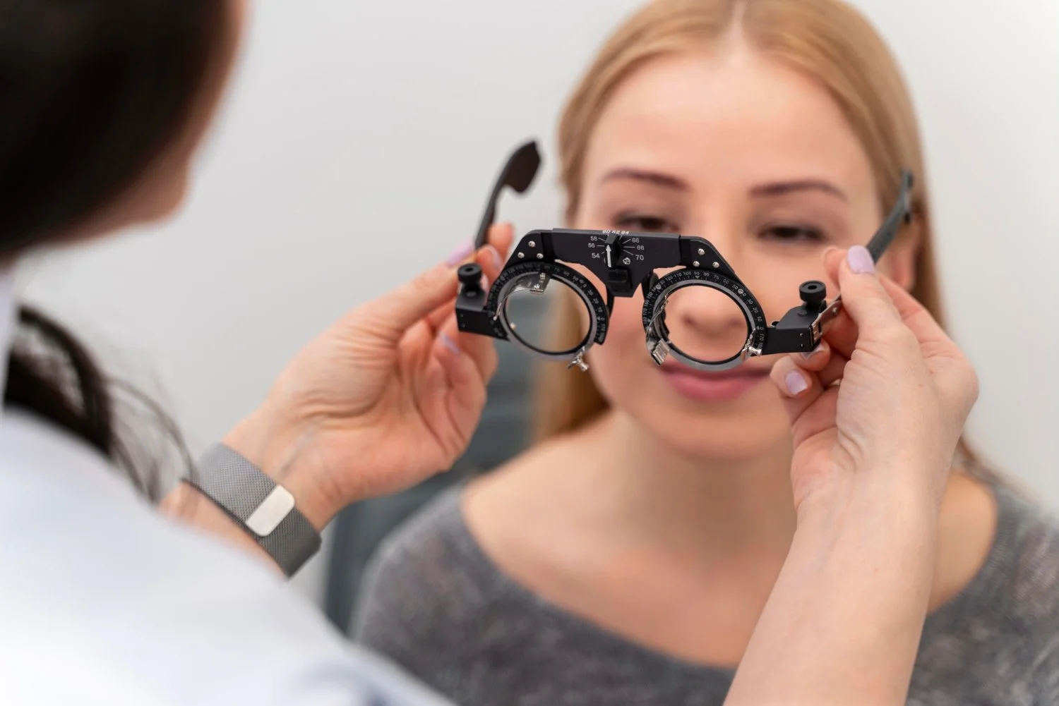 Optometrist checking woman's eyes with trial frame.