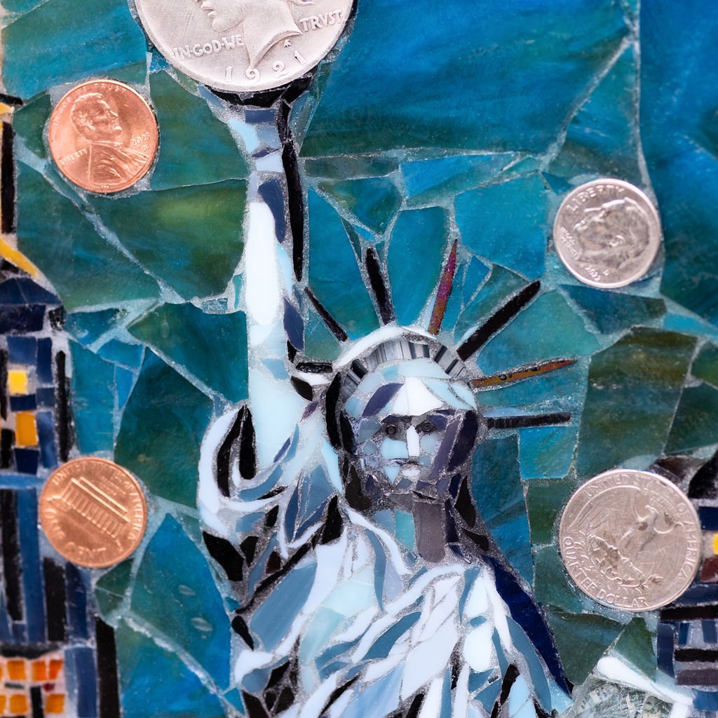 Mosaic artwork of the Statue of Liberty's face and torch, with US coins (pennies, nickels, quarters) placed on the mosaic.
