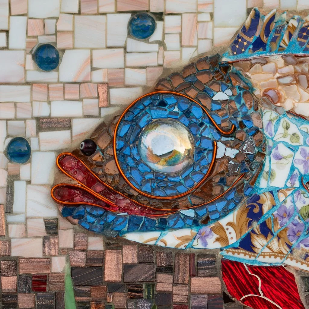 A close-up of a colorful glass mosaic art piece featuring a chameleon, with a detailed tail and eye, set against a tiled background.