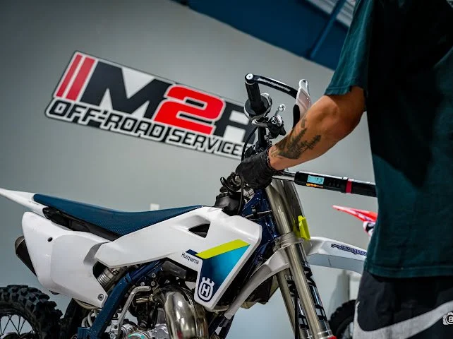 A tech is working on a Husqvarna 2 Stroke dirt bike at M2R OffRoad Suspension.