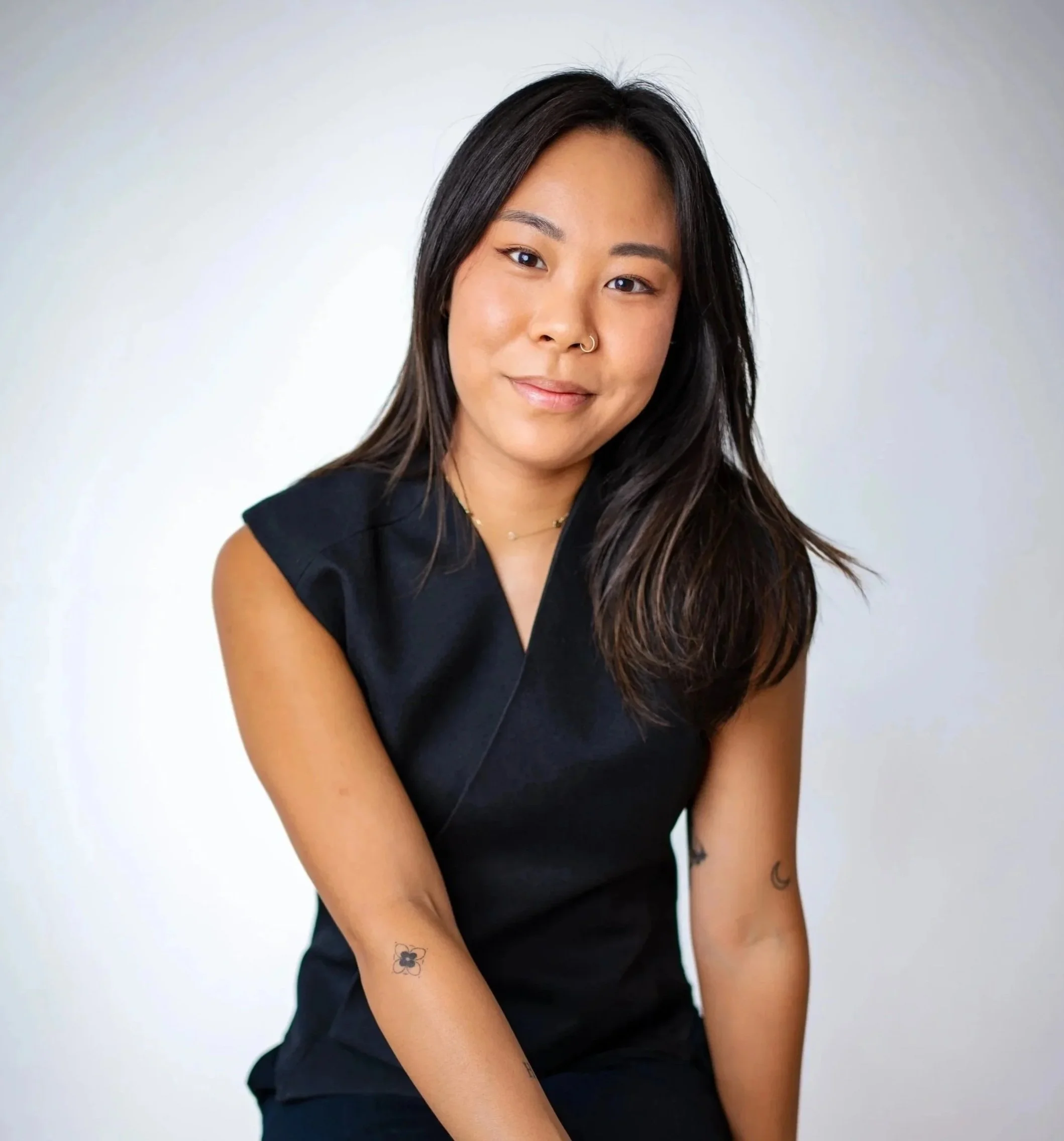 A young woman with dark brown hair, wearing a sleeveless black top, smiling slightly, against a plain white background.