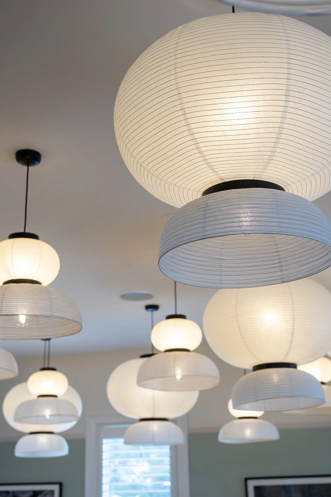 Multiple white paper lantern pendant lights hanging from the ceiling in a modern interior space.