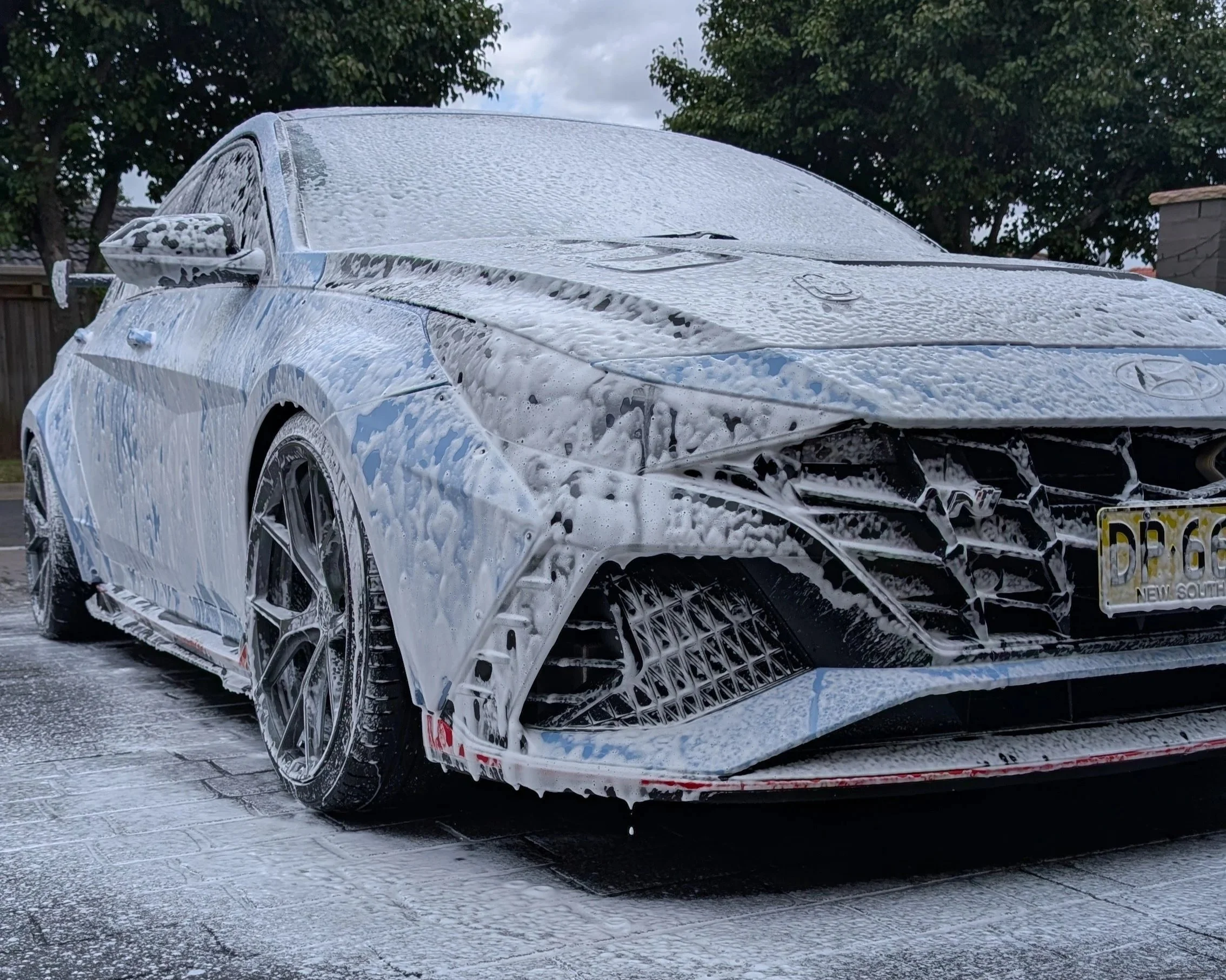 "Silver car covered in soap suds during a professional car wash in Sydney