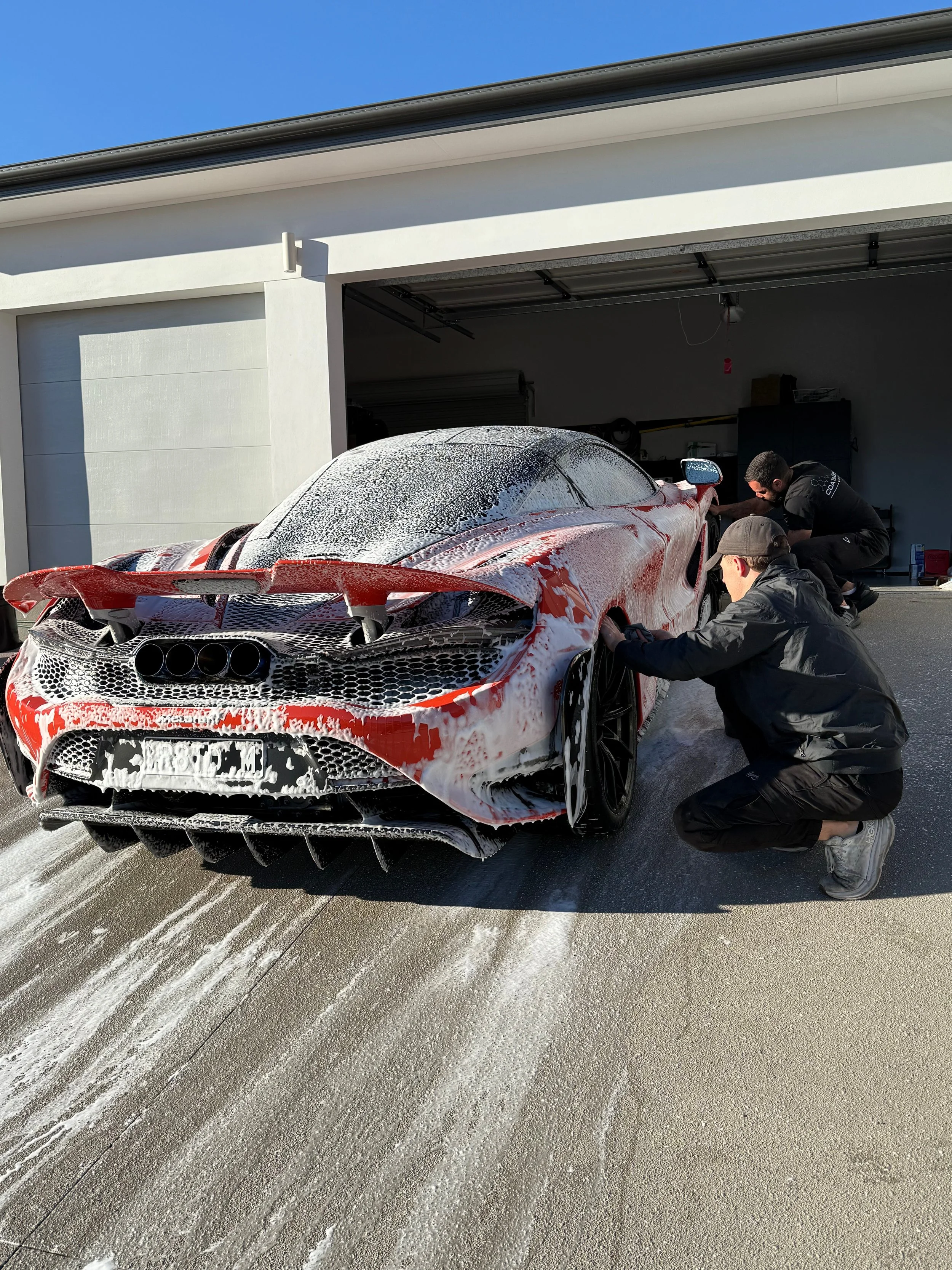 Coatings Lab team hand-washing a red race car before ceramic coating application