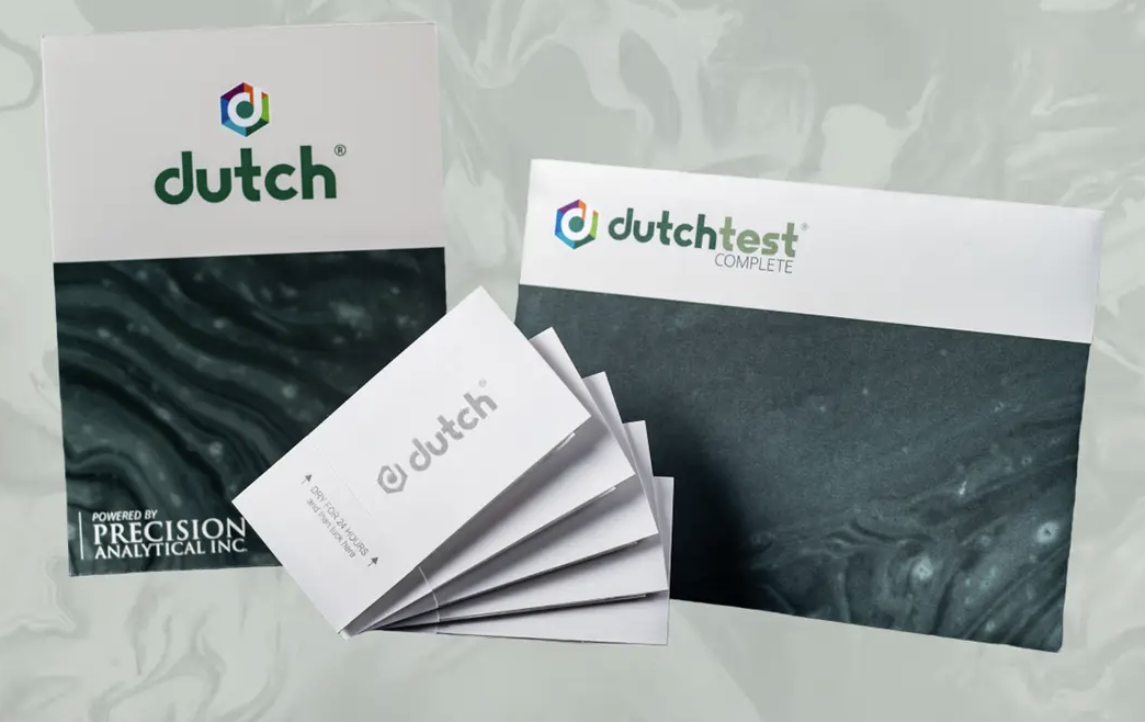 Multiple health-related documents and a kit box labeled 'dutchplus' from Precision Analytical Inc. on a dark surface.