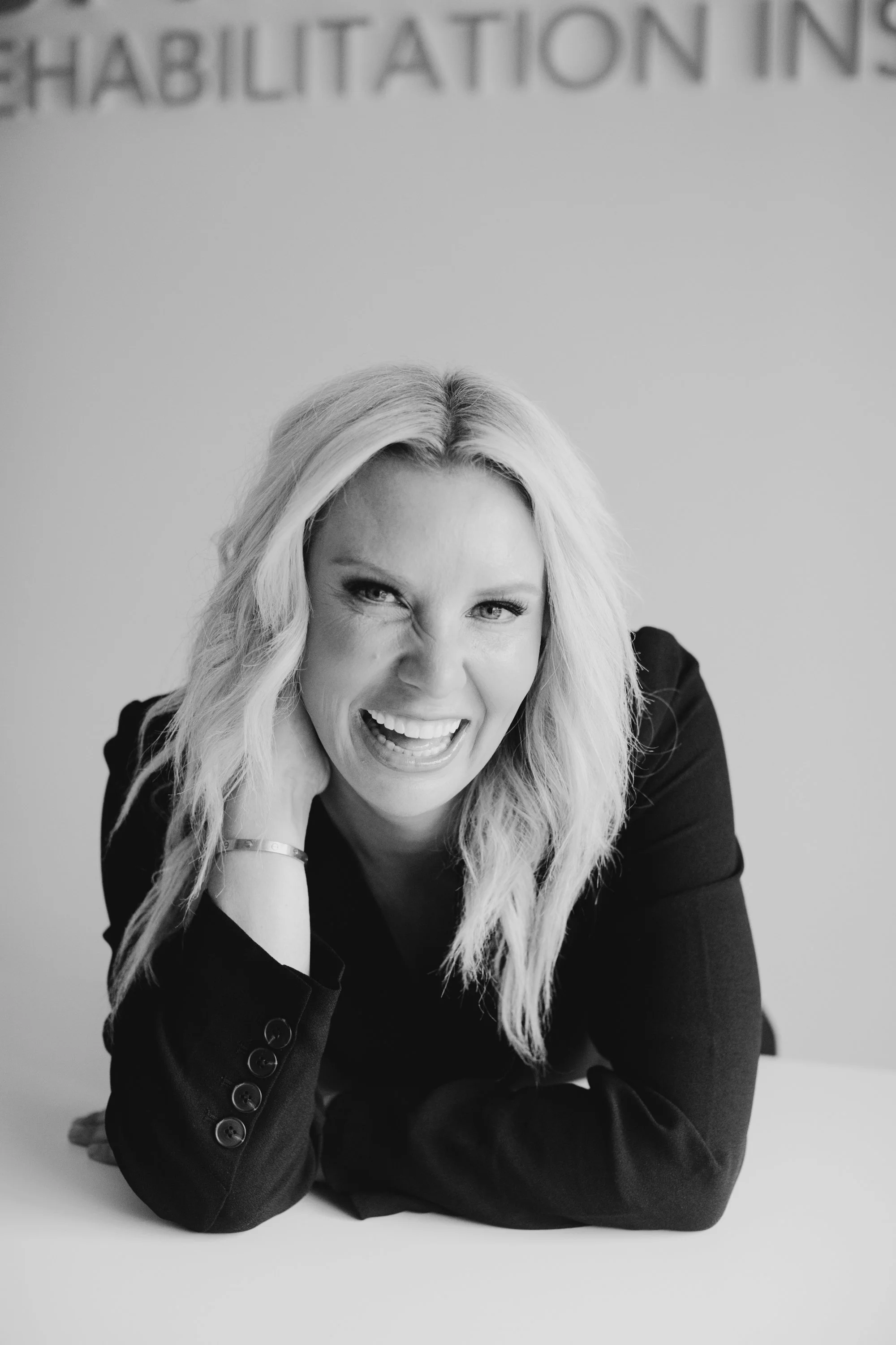 Black and white photo of Dr. Audra Lance smiling and leaning on a table, wearing a dark blazer.
