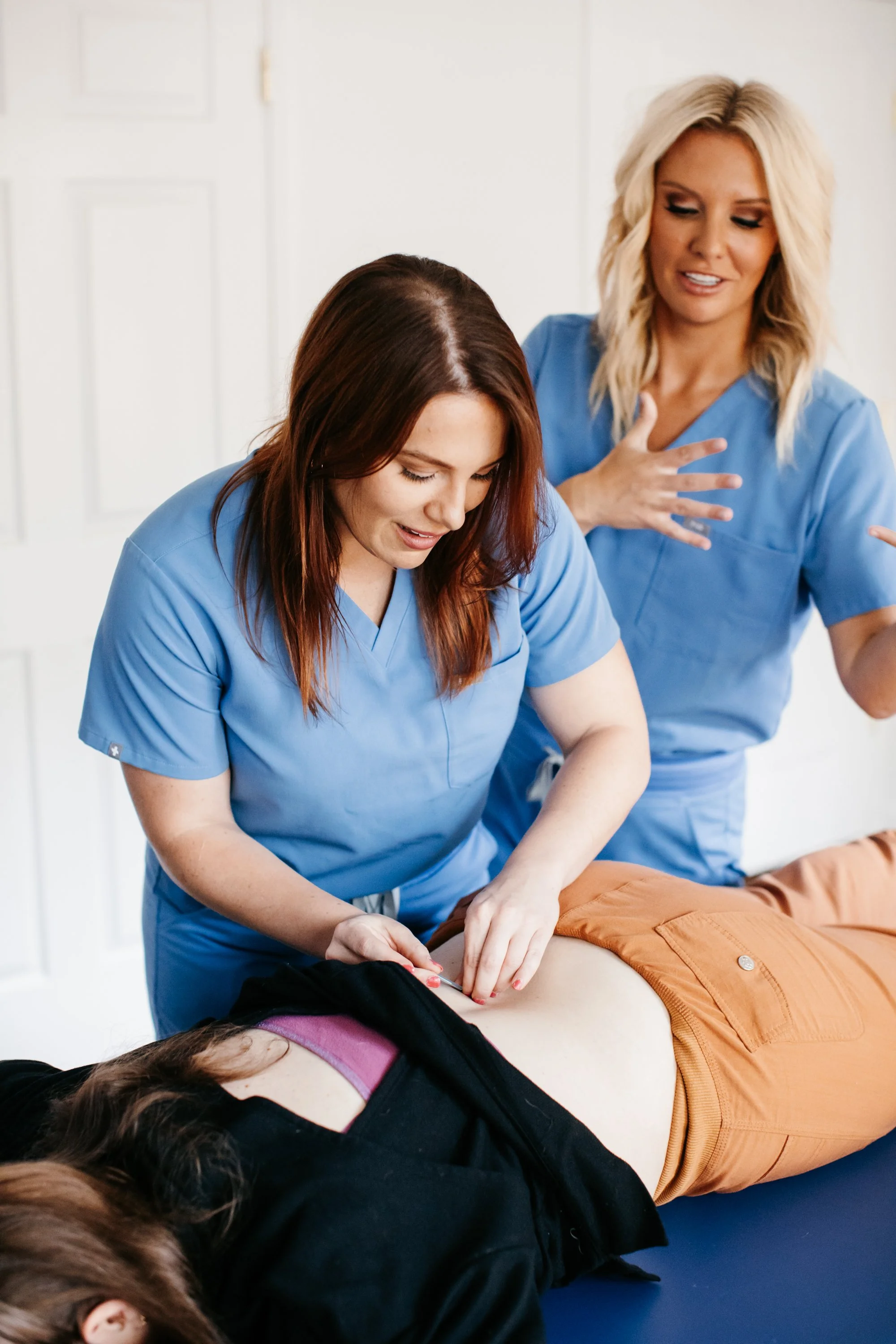 Two healthcare professionals in blue scrubs performing chiropractic work on a woman lying on a medical table.