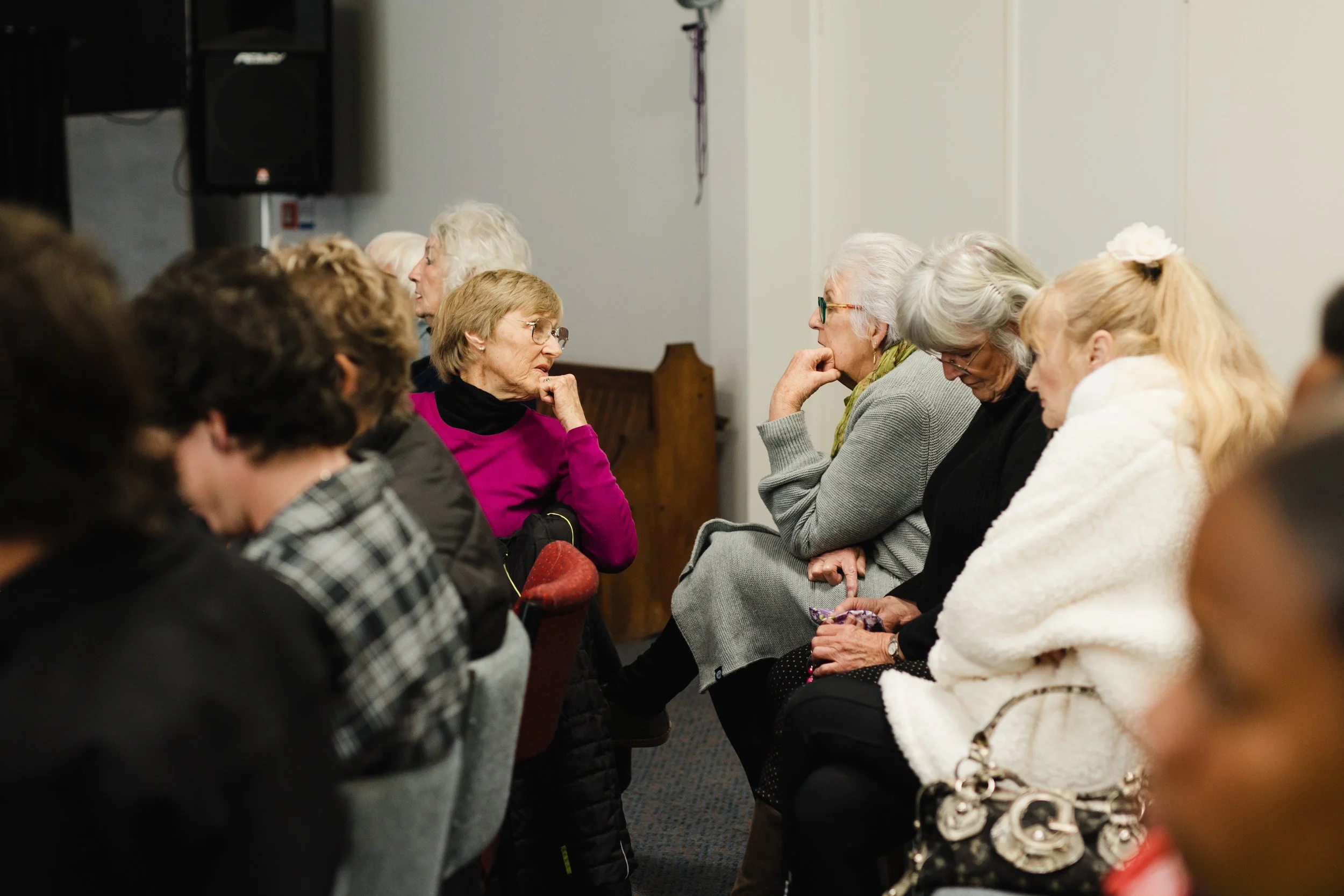 A group of people sitting in a row, engaged in conversation and listening attentively in an indoor setting.