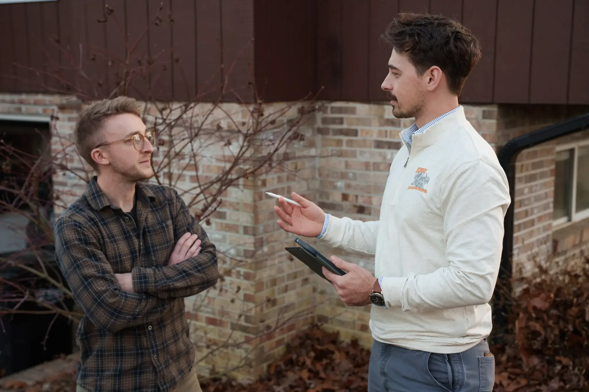 Knox Exterior Care Co. owner and a customer standing outside a brick property during a consultation, one in a plaid shirt and one in a KECC-branded white pullover