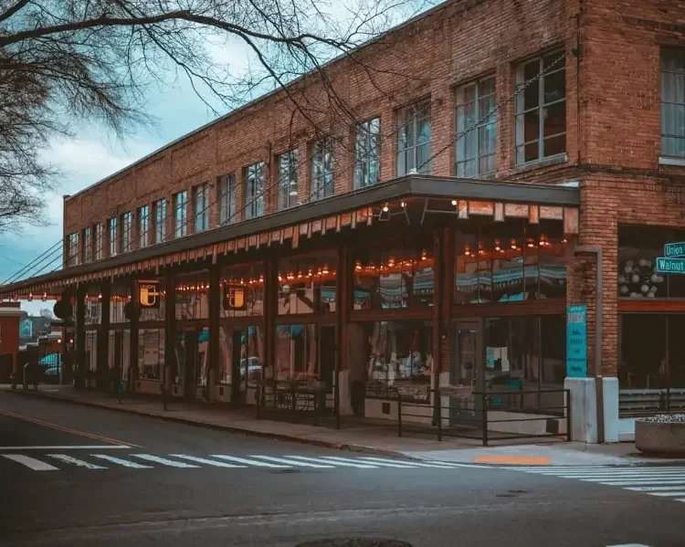Brick commercial building exterior in Knoxville, TN at dusk with warm string lights on the patio, bare winter trees, and a street-level view — representing KECC's commercial exterior maintenance services