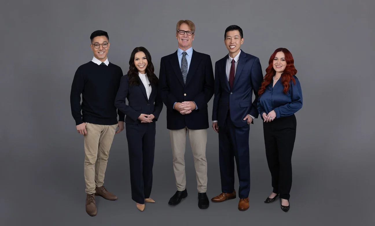Group of five diverse professionals standing together in business attire against a gray background.