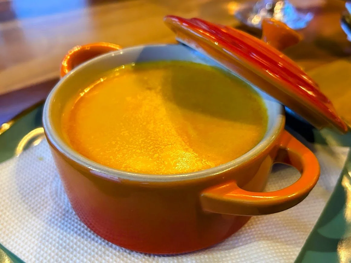 A ceramic cup with a lid containing a yellow-colored soup placed on a white napkin on a green tray.