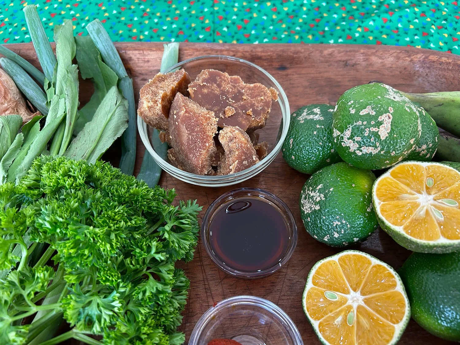 Fresh green limes, halved and whole, along with lemongrass, dried brown sugar, and green herbs on a wooden tray.