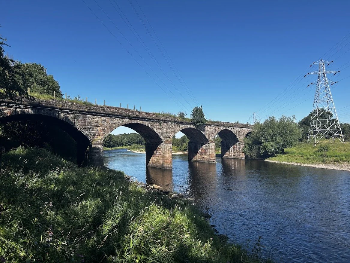 countryside view with stone bridge over river by green field and blue skies