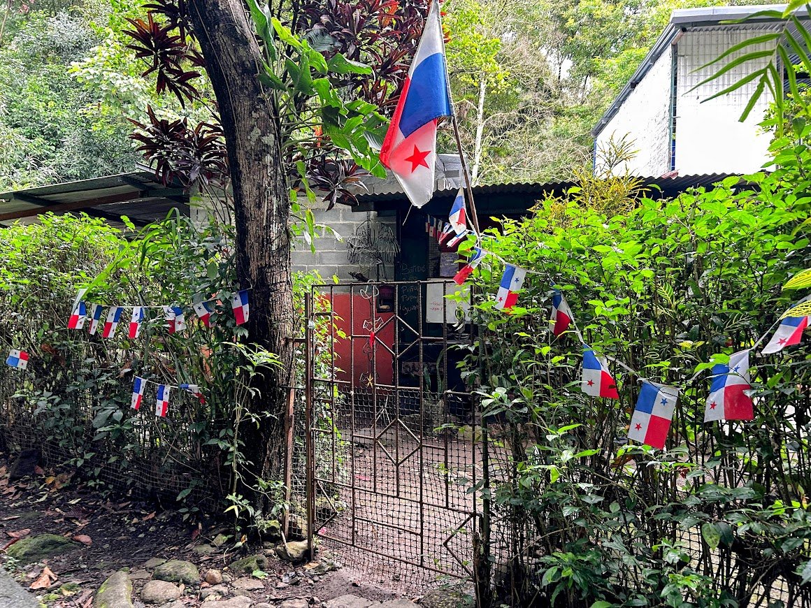A garden entrance decorated with French and Panamanian flags, surrounded by lush green bushes and trees.