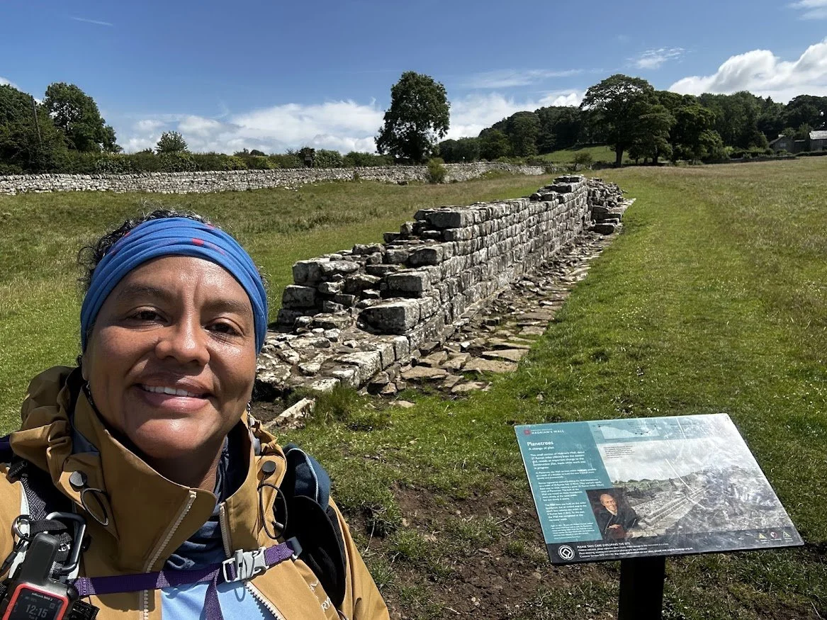 woman hiker in front of hadrians wall section in field countryside and signpost