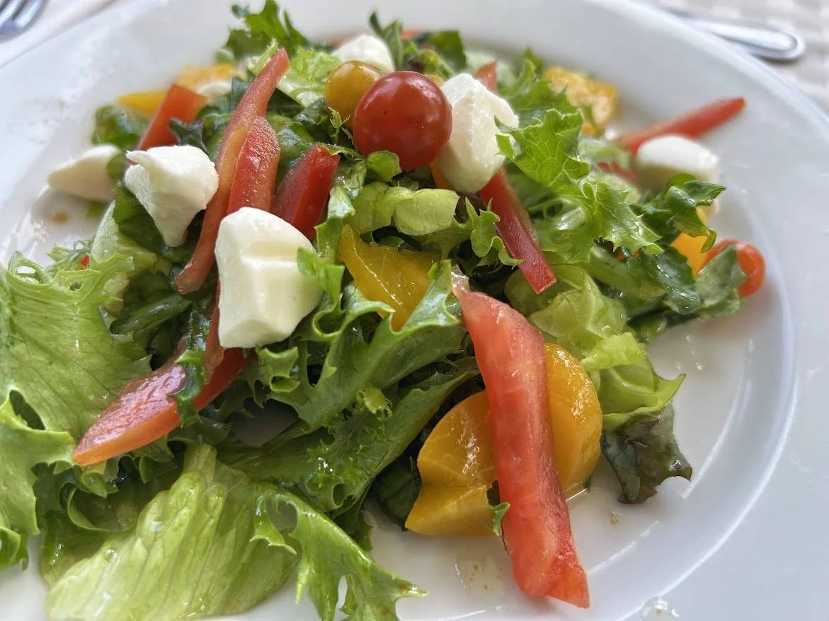 Fresh garden salad with leafy greens, cherry tomatoes, bell pepper strips, and mozzarella cheese on a white plate.