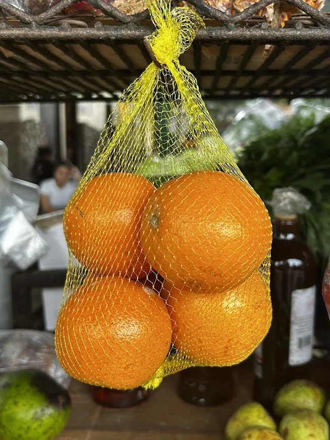 Four oranges in a yellow net bag hanging in a market or grocery store.