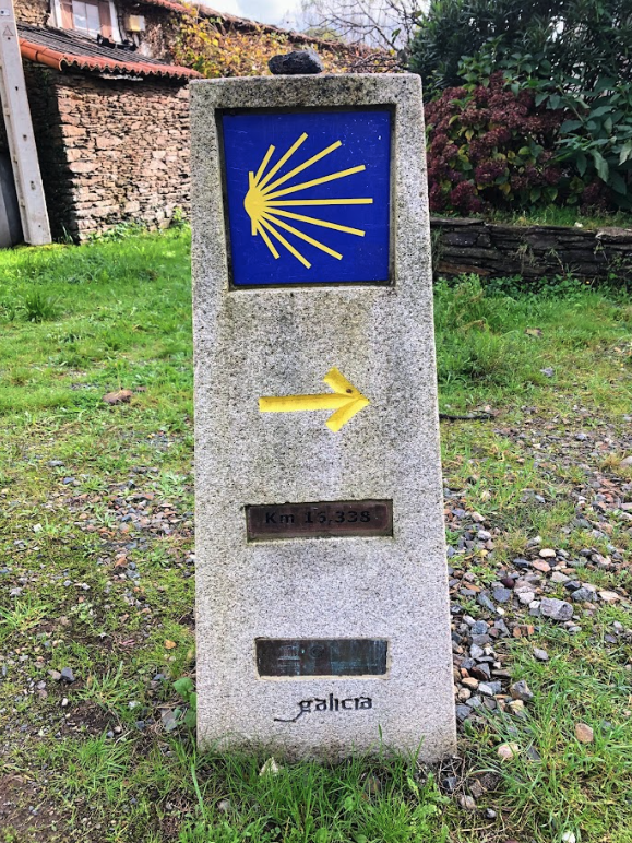 camino de Santiago way marker with yellow shell sign and yellow arrow in grassy ground