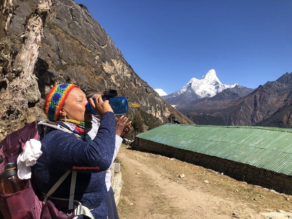 woman drinking water in mountain nepal with green roof building and blue skies