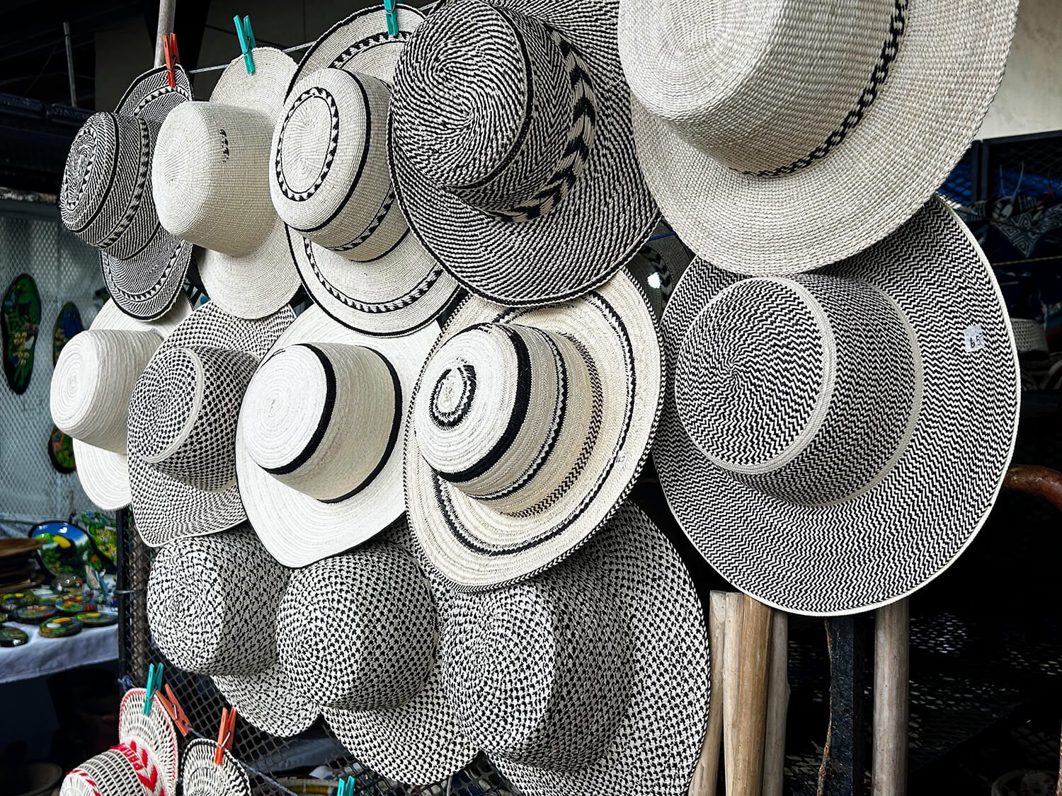 Collection of black and white woven hats with various patterns hanging on a display rack at an outdoor market.