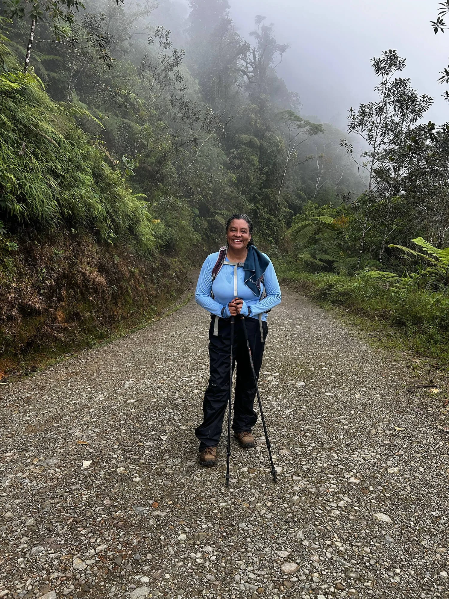 woman hiker happy standing in the misty forest on a gravel road with hiking poles