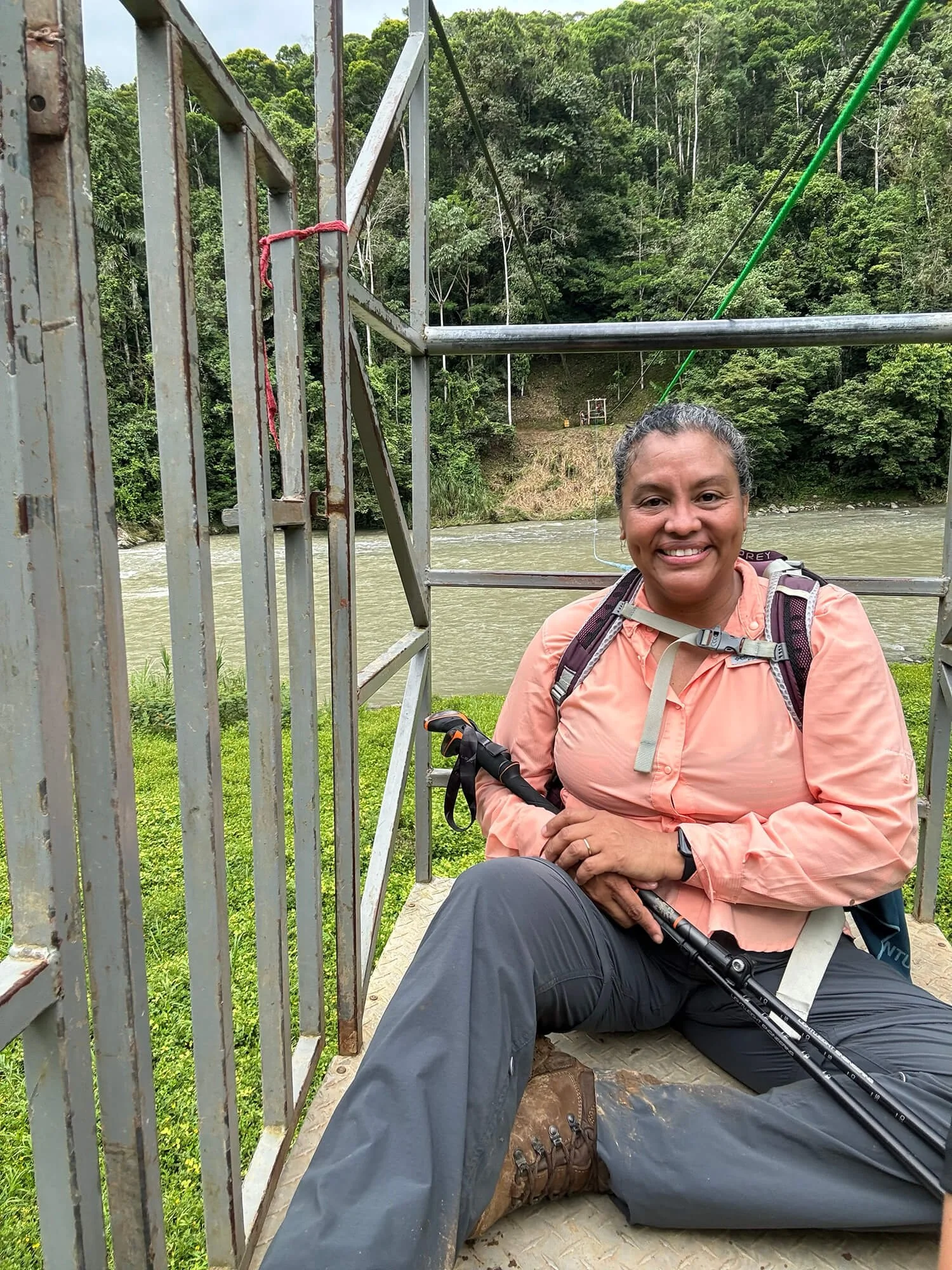 woman hiker in transport cage over river hiking poles backpack happy