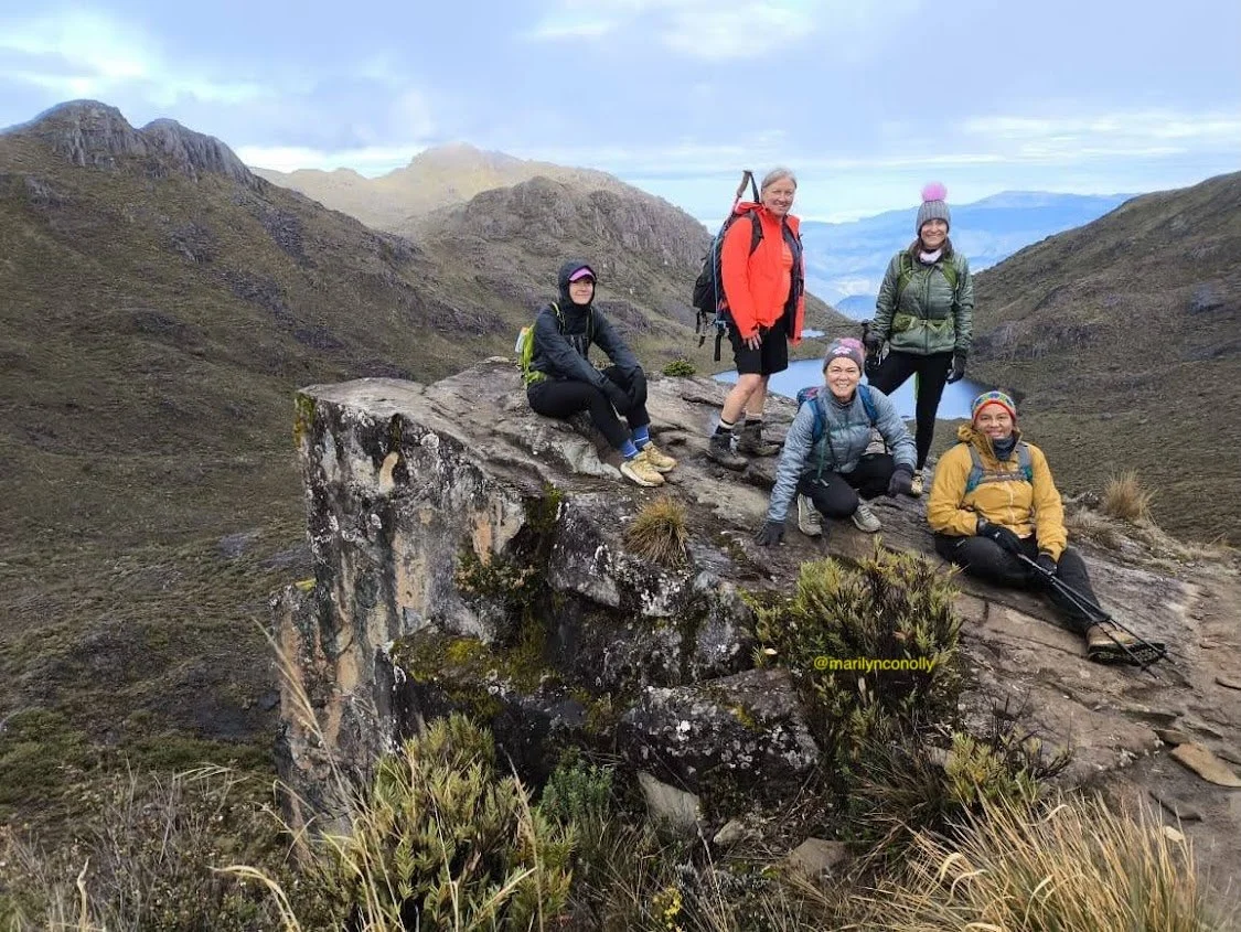 happy women hikers smiling on rocky outcrop over mountainous landscape
