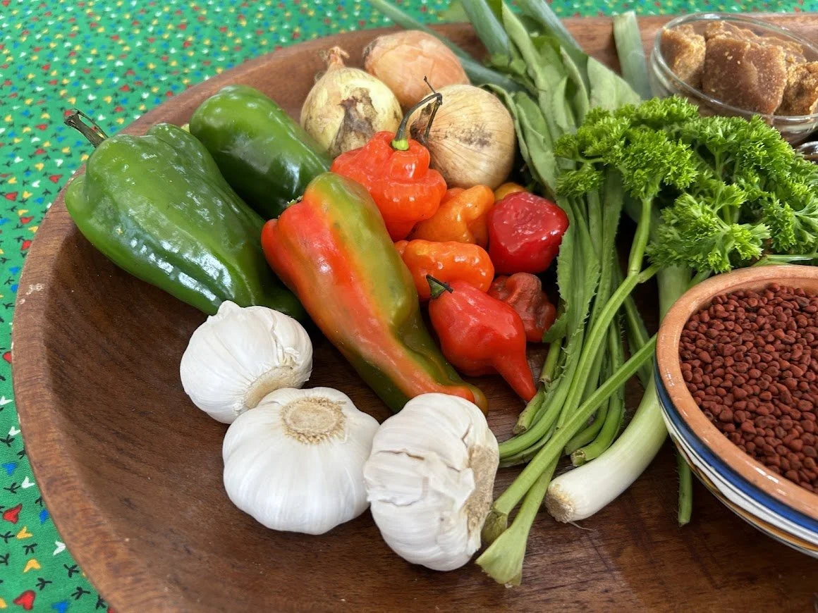 Assorted fresh vegetables including green and red peppers, garlic, onions, green beans, parsley, and chili peppers on a wooden platter.
