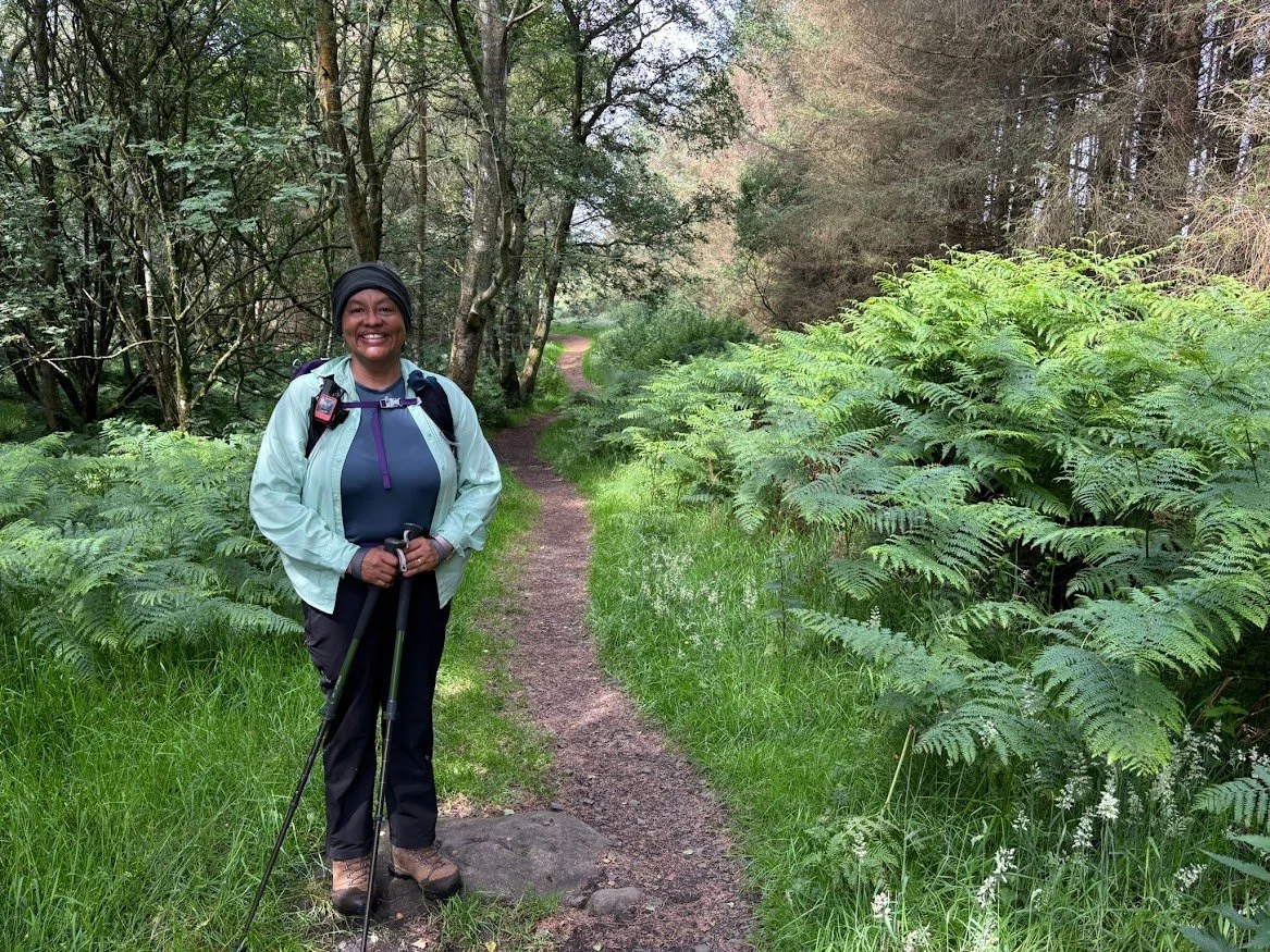 woman hiker on forest trail lush greenery and trees with hiking poles