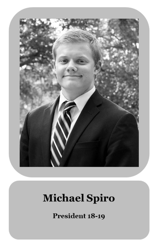 Black and white portrait of Michael Spiro in a suit and striped tie, outdoors with trees in the background, smiling