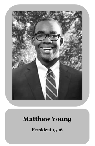 Black and white photo of Matthew Young, president for the 2015-2016 year, wearing glasses, a suit, and a striped tie, outdoors with trees in the background.