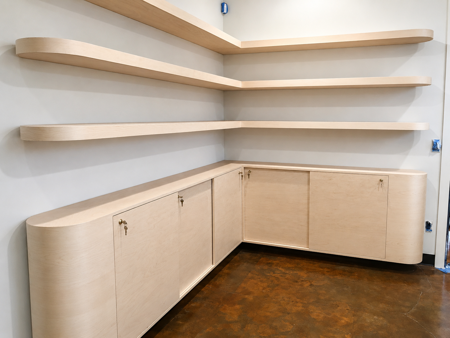 Empty built-in wooden cabinets and floating shelves in a room with white walls and a dark brown floor.