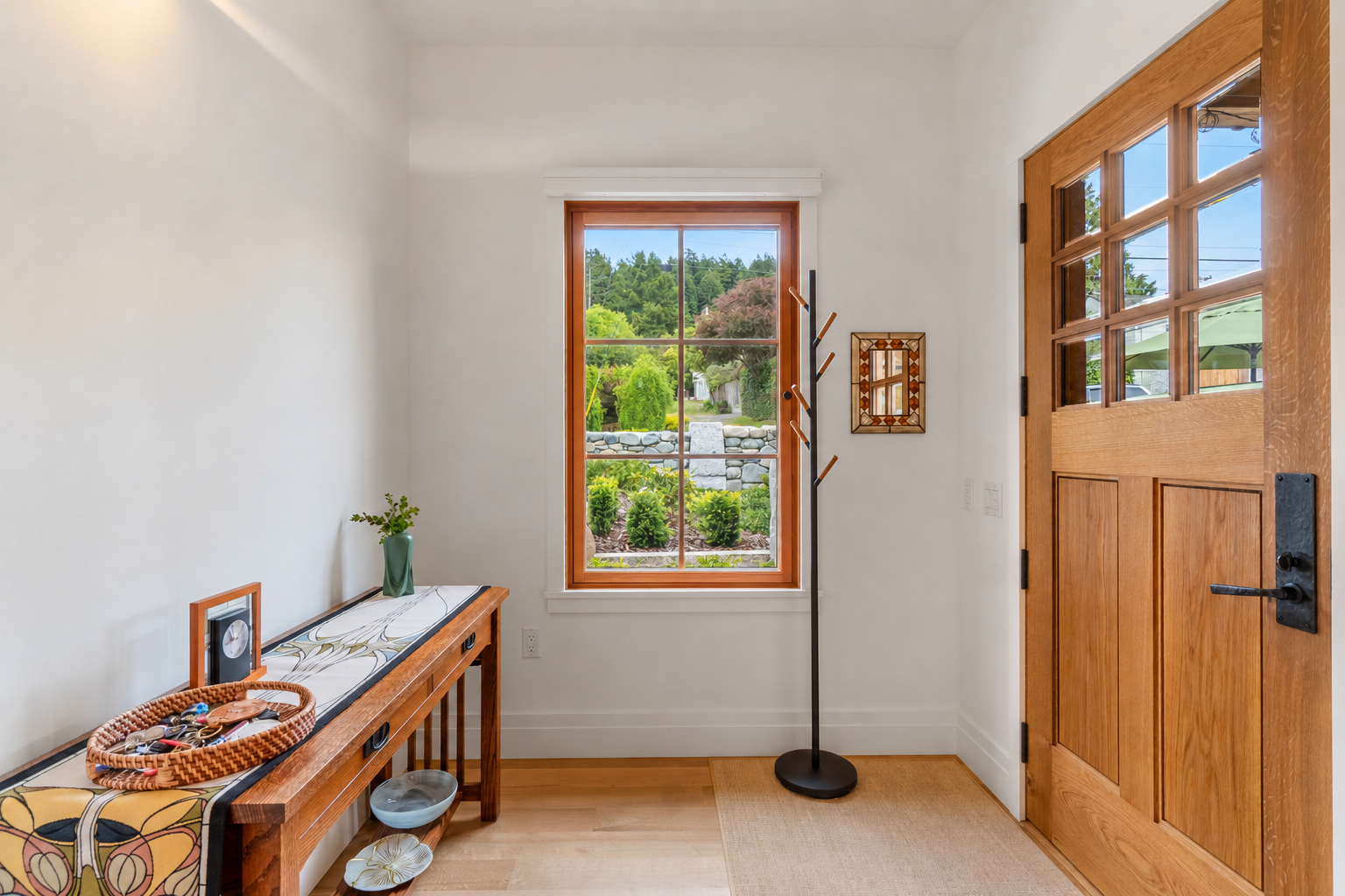 Entryway with wooden door, window showing outdoor garden, coat rack, and decorative wall mirror.